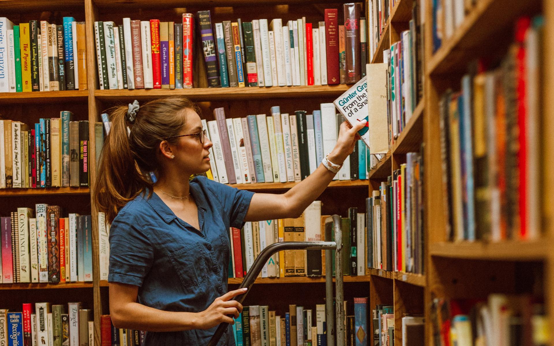 Junge Frau auf einer Leiter vor dem Bücherregal