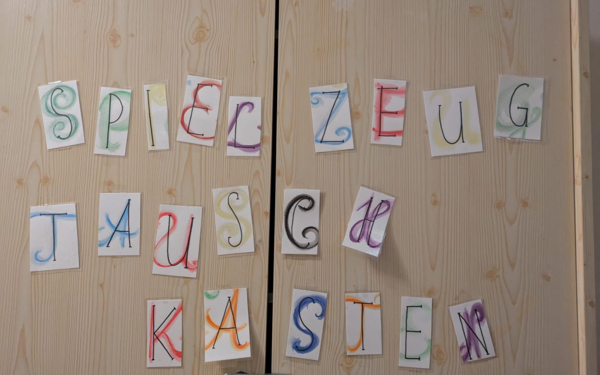 Tür mit bunt gestalteten Buchstaben, die das Wort „Spielzeug-Tauschkasten“ ergeben – Hinweis auf eine Tauschmöglichkeit für Kinderspielzeug.