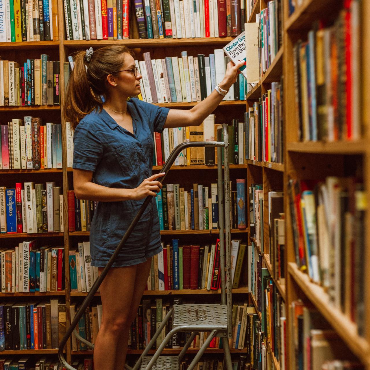 Junge Frau auf einer Leiter vor dem Bücherregal