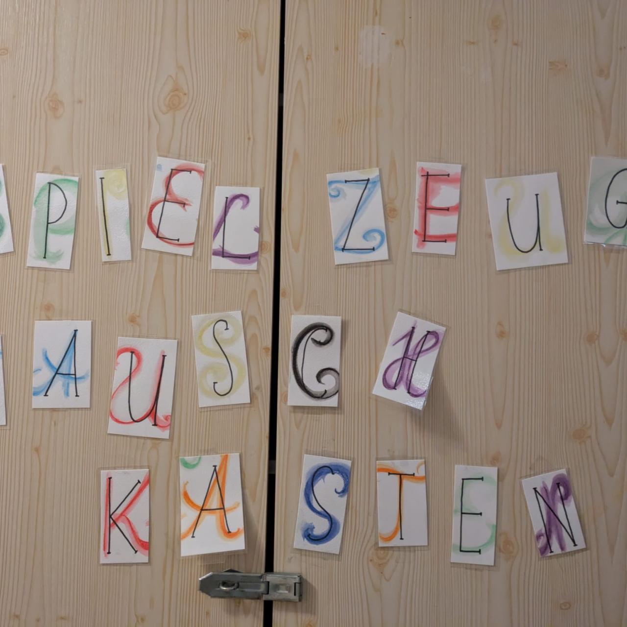 Tür mit bunt gestalteten Buchstaben, die das Wort „Spielzeug-Tauschkasten“ ergeben – Hinweis auf eine Tauschmöglichkeit für Kinderspielzeug.